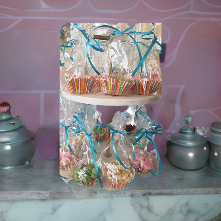 Clear plastic candy bags with assorted candies visible inside, tied with blue ribbons, displayed in front of a pink background.