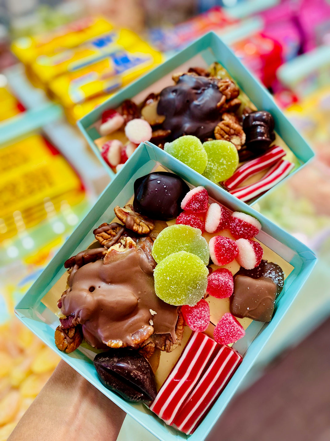 Two small boxes filled with assorted candies and chocolates on a colorful background.