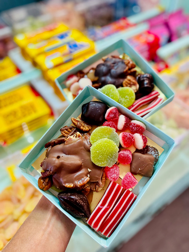 Two small boxes filled with assorted candies and snacks held by a person.