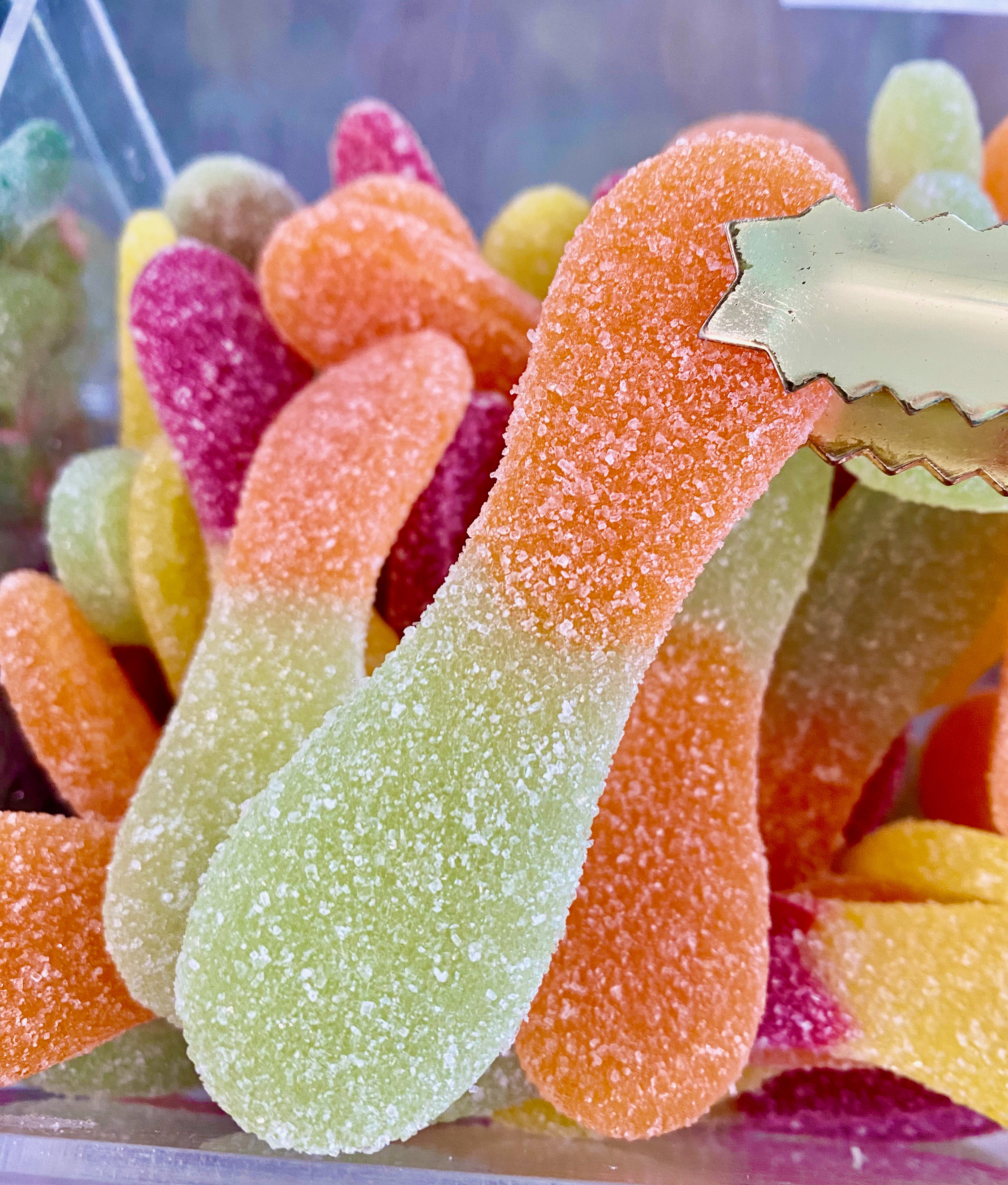 Colorful gummy tongue candy in a clear container with a metal scoop.