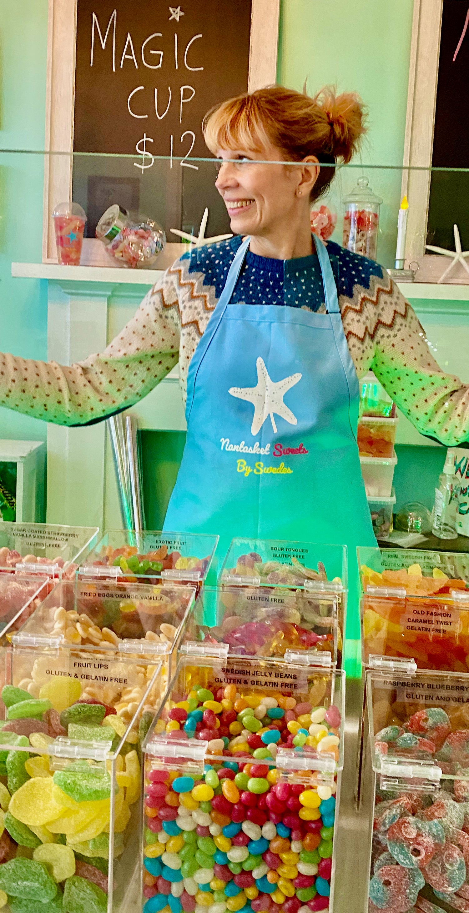 Woman in a candy store with colorful candies and a blue apron.