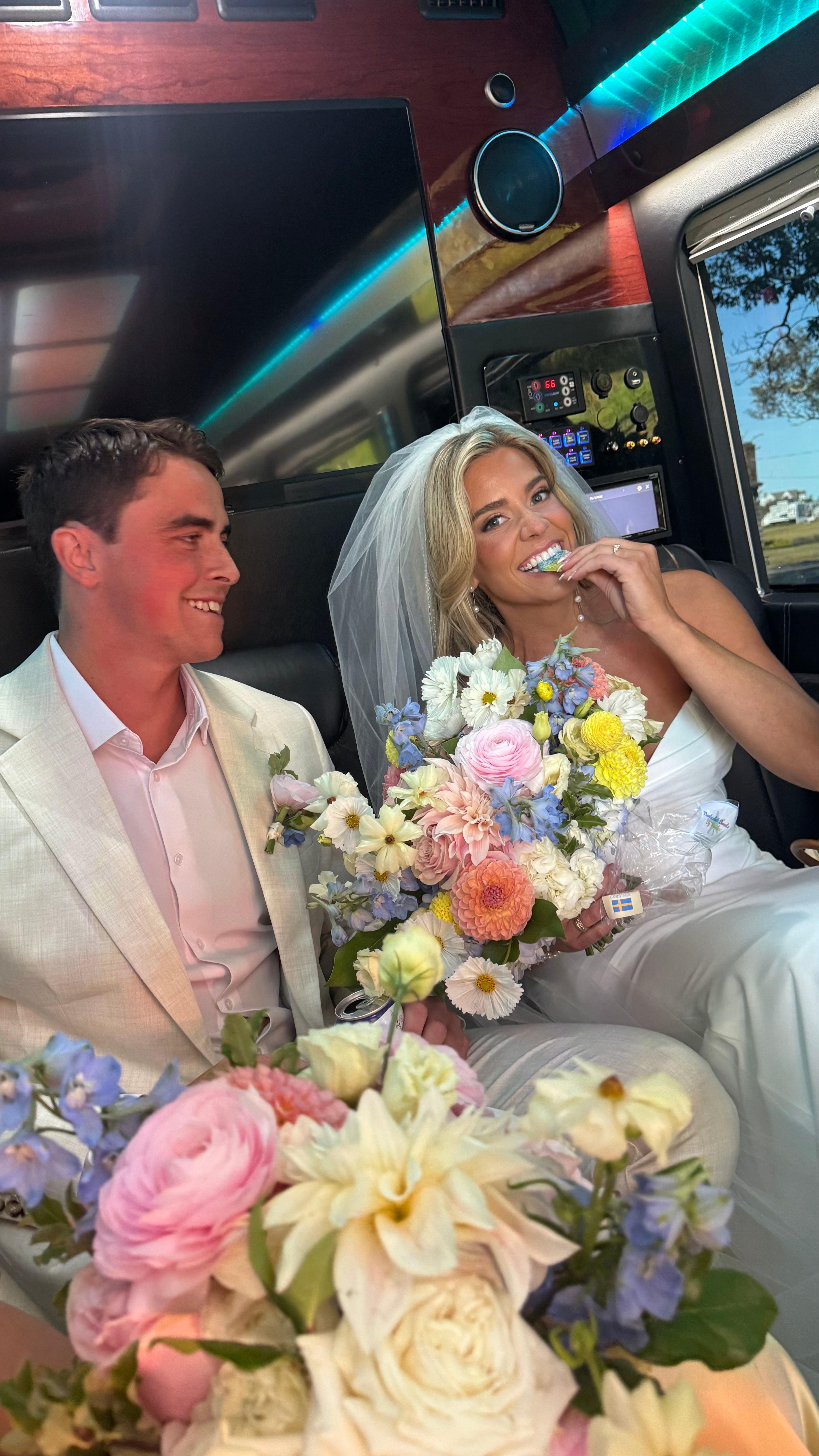 Man and woman in wedding attire with floral bouquets inside a limousine.