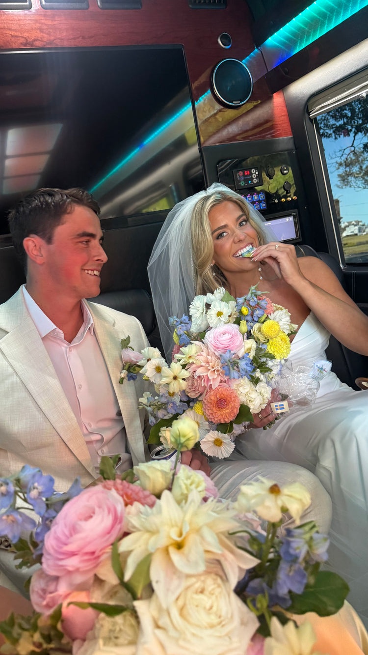 Man and woman in wedding attire with floral bouquets inside a limousine.