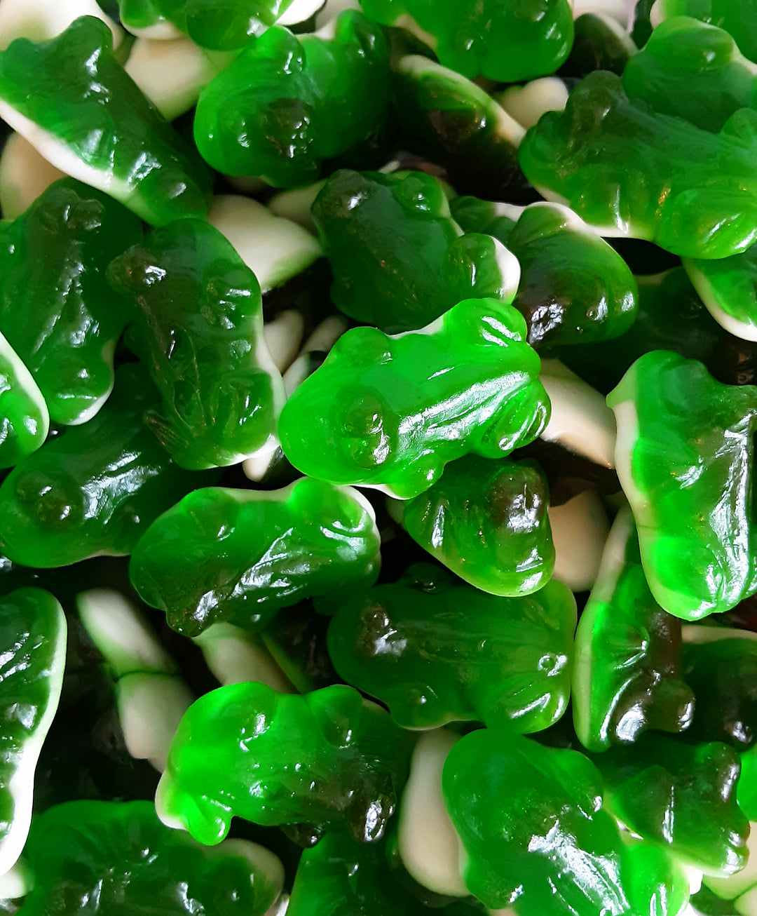 Close-up of green gummy bears and white candy pieces.
