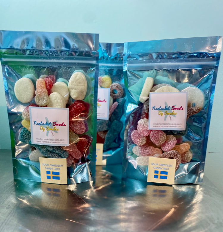 Two packages of Swedish Sweets by Snacks on a reflective surface with a light blue background.