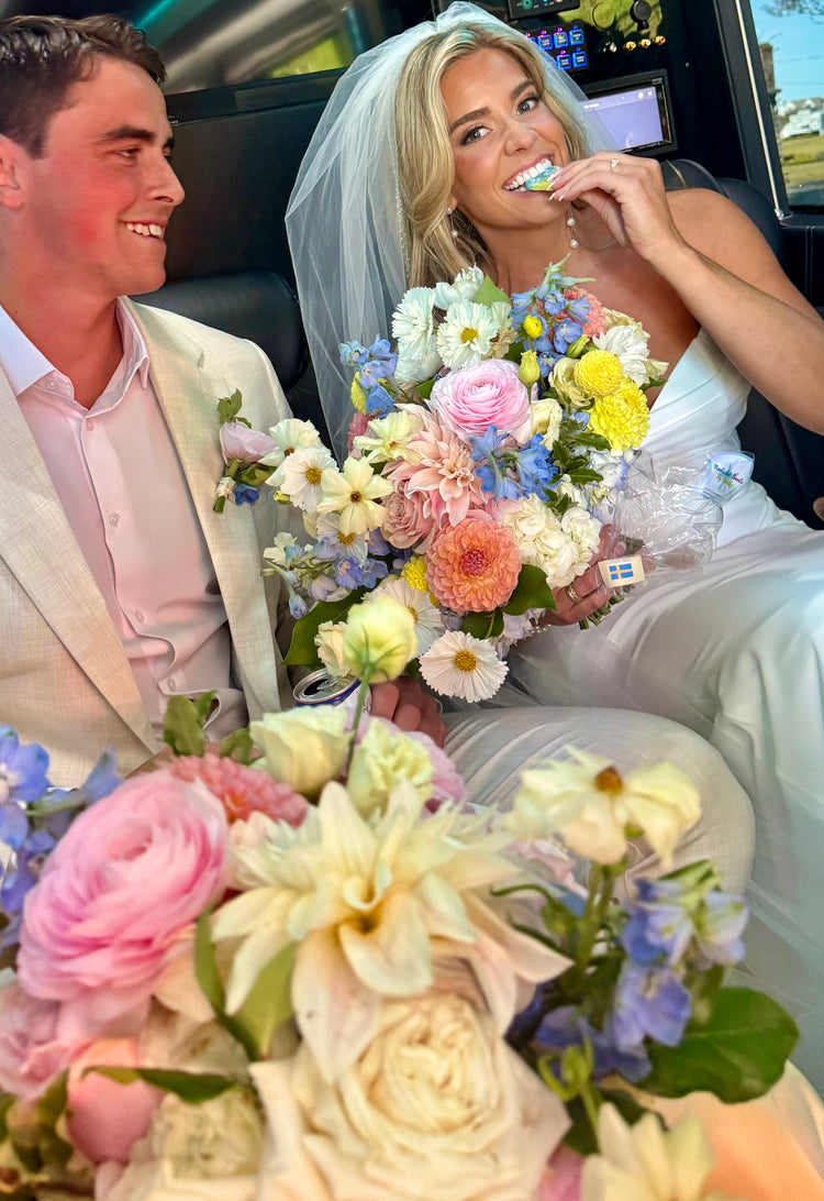 Woman in a wedding dress holding a bouquet of flowers, sitting next to a man in a suit inside a car.